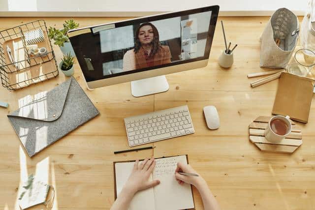 Cómo estudiar a distancia por internet. Mujer toma apuntes desde su casa para su clase a distancia por internet.