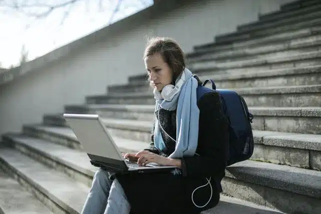 Estrategias para estudiar a distancia. Chica estudiando frente al ordenador sentada en la calle.