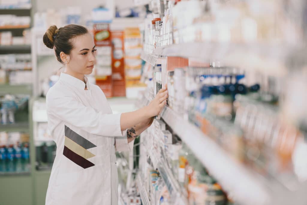 medicine pharmaceutics health care and people concept female pharmacist taking medications from the shelf